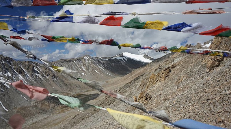 Colourful prayer flags waving in the wind against an impressive mountain landscape under partly cloudy sky, trekking in Ladakh, Himalayas, India