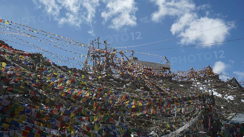 A network of colorful prayer flags stretched at Khardung-La Pass under a blue sky, trekking in Ladakh, Himalayas, India