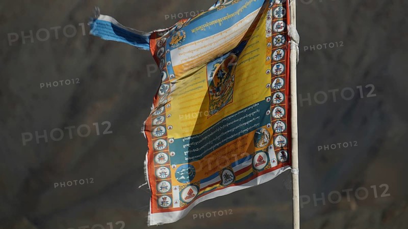 Colourful Tibetan prayer flag moving in the wind in front of a rocky mountain, trekking in Ladakh, Himalayas, India