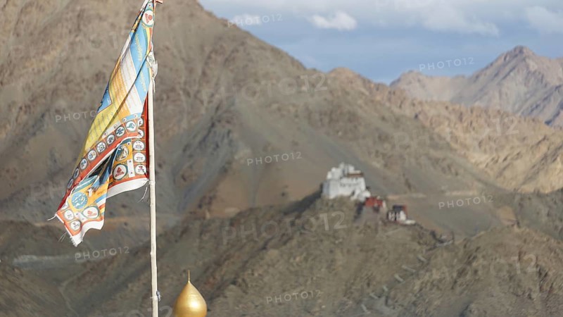 Colourful Buddhist flag against a mountain backdrop with Namgyal Tsemo monastery in the distance, Leh, trekking in Ladakh, Himalayas, India
