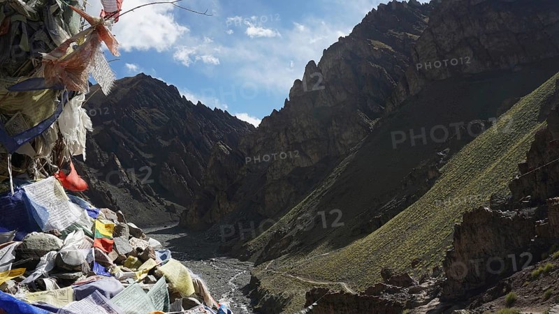 View of a valley with prayer flags and barren mountain landscape under blue sky, trekking at Stok La Pass in Ladakh, Himalayas, India