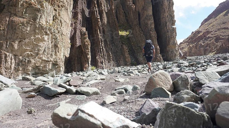 A hiker with a backpack walks through a rocky gorge under a blue sky, trekking at Stok La Pass in Ladakh, Himalayas, India