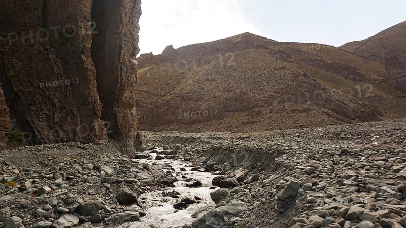 A stream flows through a dry, rocky landscape with high rock walls, trekking at Stok La Pass in Ladakh, Himalayas, India