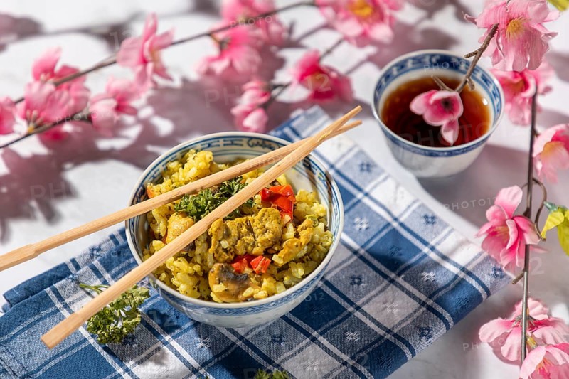 Chinese bowl with rice and vegetables next to tea, decorated with cherry blossoms