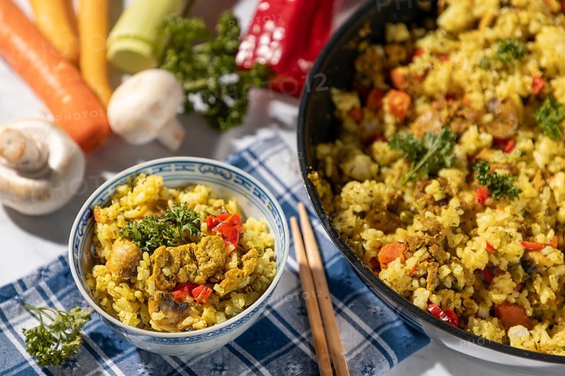 Bowl of fried rice and chopsticks next to pan and fresh ingredients