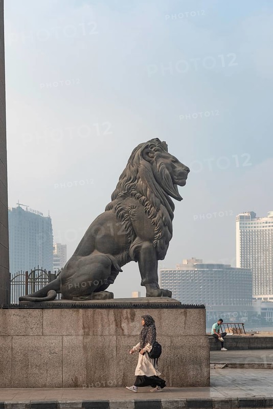 Cairo, Egypt. July 1st 2024 A woman walks past one of the famous bronze lions guarding Qasr El Nil Bridge over the River Nile in Downtown Cairo, Egypt
