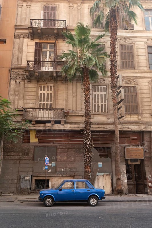 Cairo, Egypt. July 1st2024 A small blue car parked in an empty street of Downtown Cairo, with palm trees and typical Egyptian style architecture, Egypt