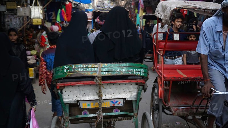A hustle and bustle of rickshaws and people passing by on a narrow street in the Muslim quarter of Delhi, India