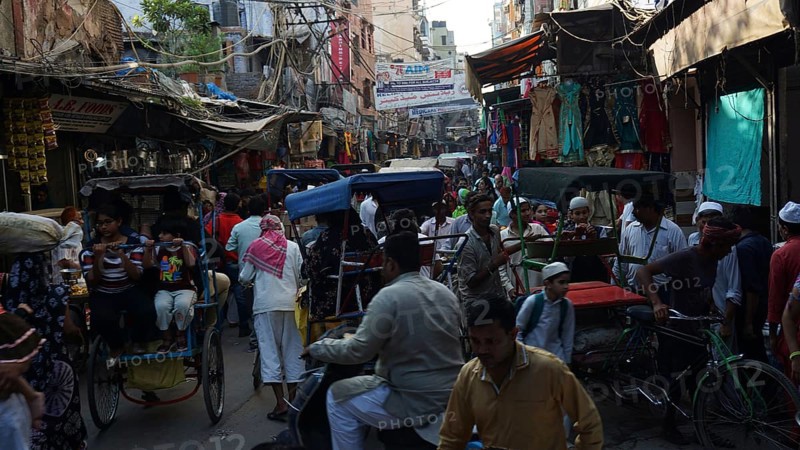 Bustling street scene with bicycle rickshaws and people in a busy market, Delhi, India