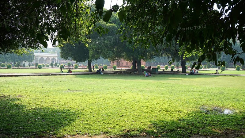 Green garden with trees in shade, people relaxing on the lawn of Red Fort in Delhi