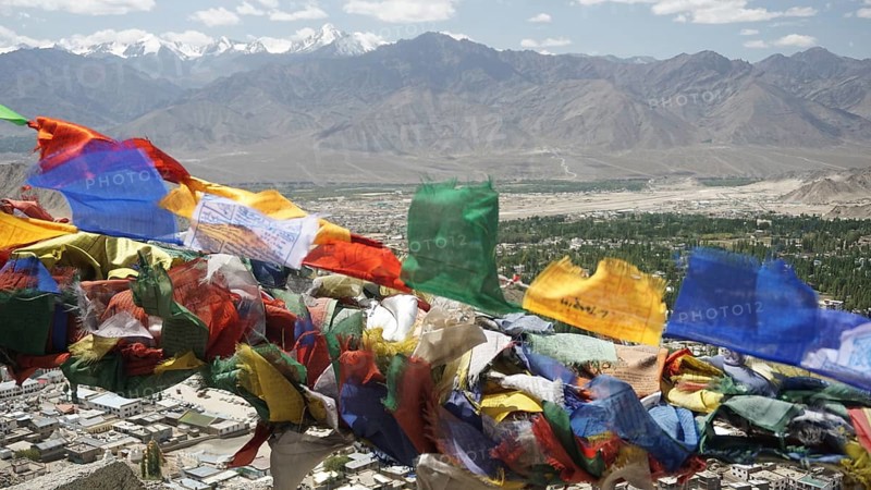 Colourful prayer flags fly over a city with mountain backdrop in the background, Leh, Ladakh, North India, Himalayas, India