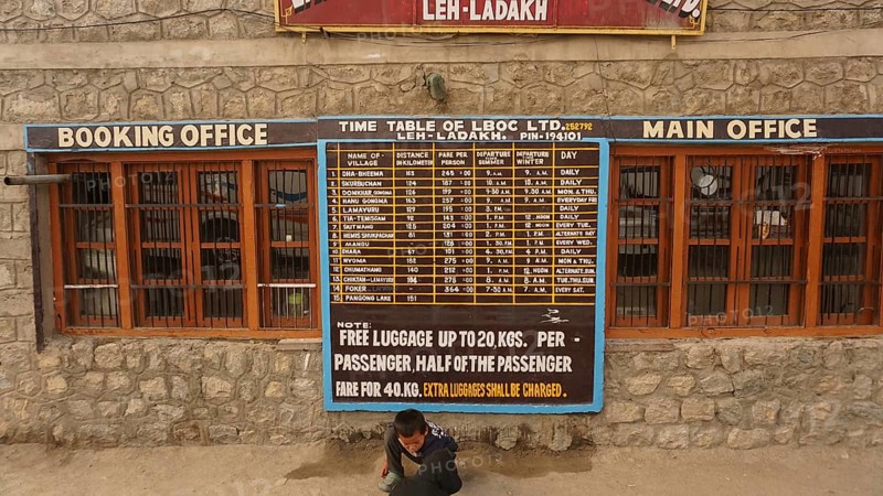 Stone building at the bus terminal with a large timetable on the façade and signs for Leh, Ladakh, North India, Himalayas, India