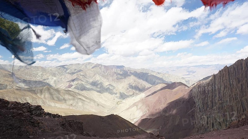 Prayer flags in front of a vast, cloud-covered mountain landscape, trekking at Stok La Pass in Ladakh, Himalayas, India