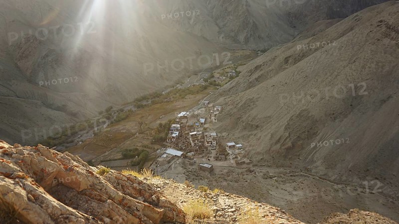 Rays of light illuminate a remote village in a valley between bare mountains, trekking in Ladakh, Himalayas, India