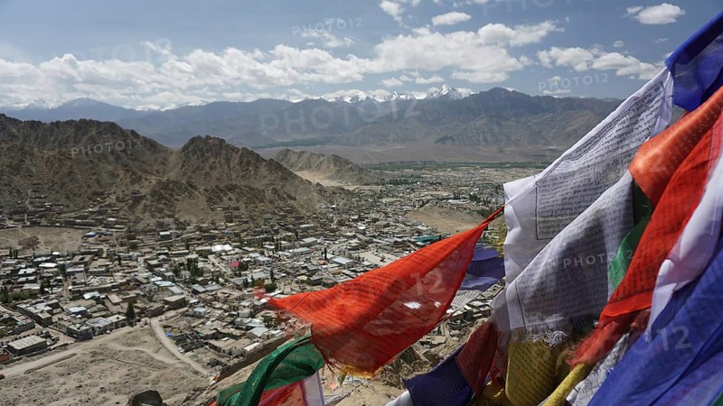 City view with prayer flags in the foreground and mountain scenery in the background under blue sky, Ladakh, Himalayas, India