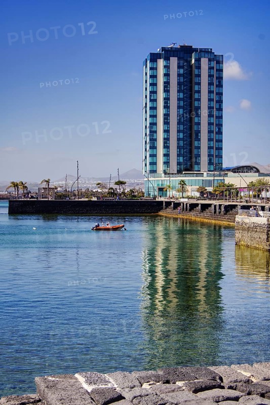 Modern high-rise building reflected in calm water, urban ambiance under clear skies, Arrecife, Lanzarote, Canary Islands, Spain