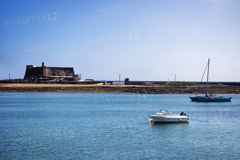 Historic Castillo de San Gabriel fortress by the sea, two boats on blue water under clear skies, Arrecife, Lanzarote, Canary Islands, Spain