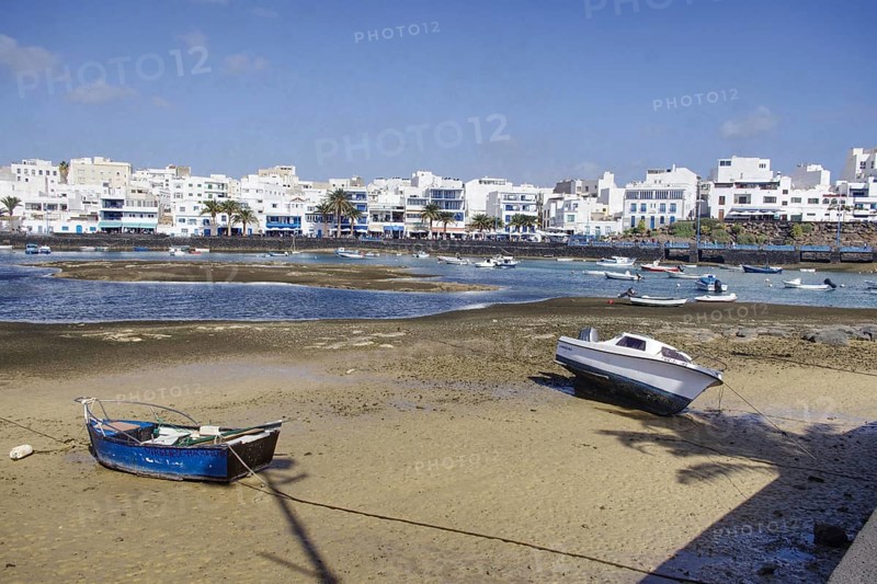 Boats on the banks of Charco de San Ginés lagoon in front of white buildings under blue sky, Arrecife, Lanzarote, Canary Islands, Spain