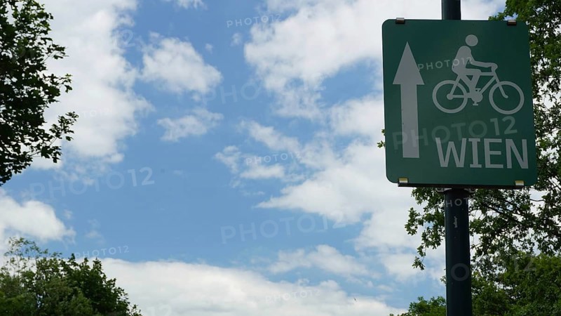 Bicycle trail sign to Vienna in front of a cloudy sky and trees, Danube Cycle Route, Austria