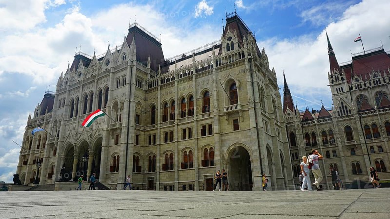 Parliament in Budapest, Impressive historic building in daylight with waving flag and people passing by, Budapest, Hungary