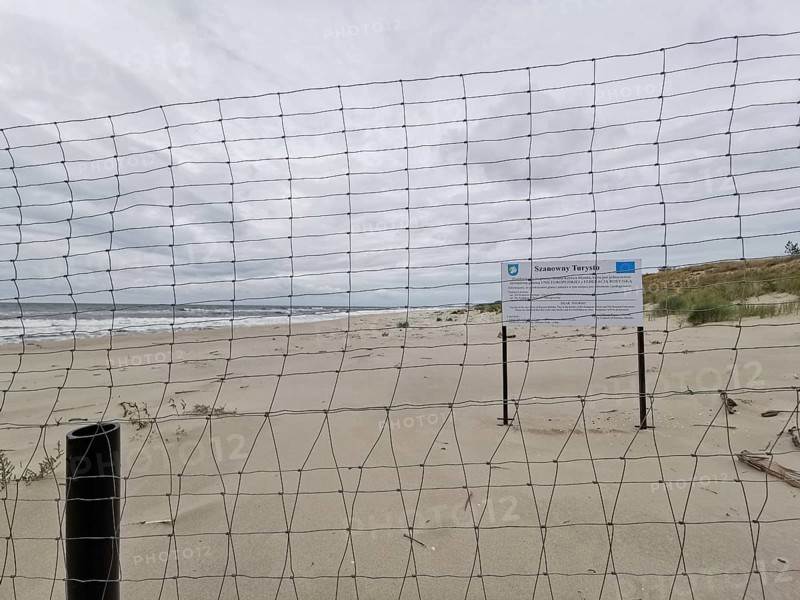 Border between Poland and the Russian exclave of Kaliningrad on the fresh spit in Poland, secluded beach with sand dunes, sea and a fence under a cloudy sky, Poland