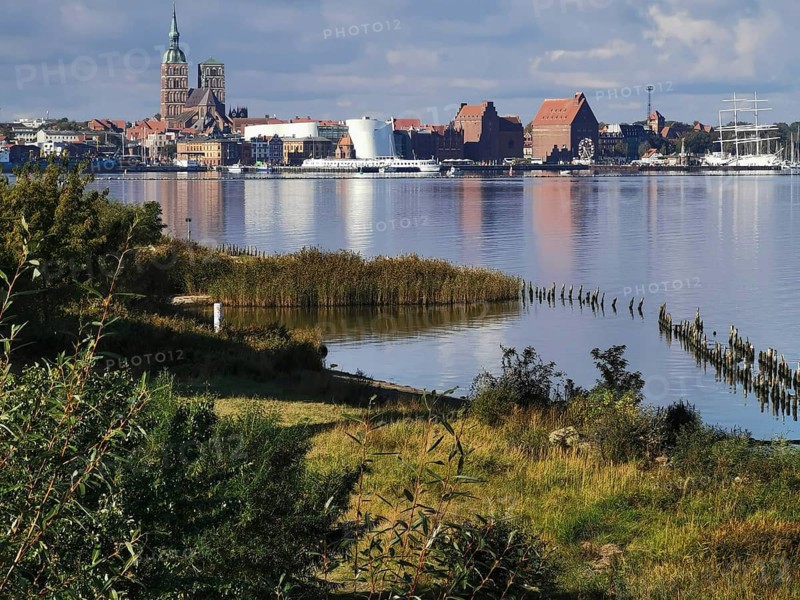 City view of Stralsund, with lakeside churches, green meadows and ships on a cloudy day