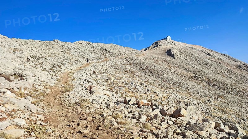 A trail snakes over a rocky mountainside up to the summit of Tahtali with clear skies, climbing Tahtali Dagi, Lycia, Turkey