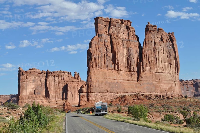 A road leads through a desert landscape with impressive sandstone formations and isolated vehicles under a clear sky, Arches National Park, Utah, USA