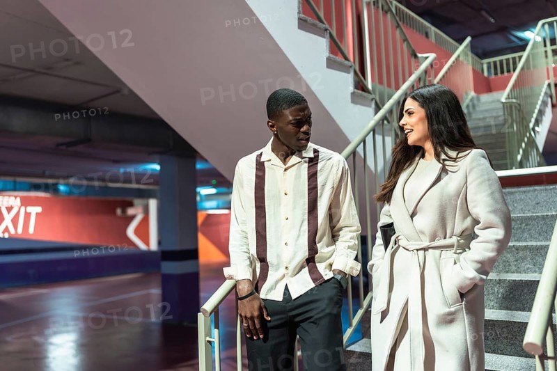 Young diverse couple walking up a concrete staircase in an underground parking facility, engaged in an animated conversation and casual interaction while moving between levels