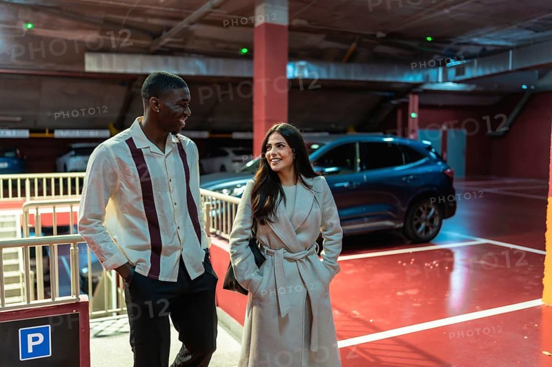 Smiling multiracial couple walking through a modern parking garage with bright red floor and cars, enjoying an urban date and candid moments of connection and joy