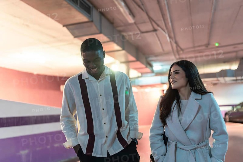 Diverse couple happily walking through an underground car park, enjoying their date while having a conversation and smiling, creating a sense of togetherness and urban lifestyle