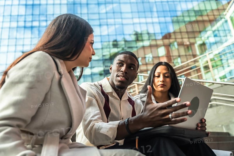 Diverse business team meets outdoors in an urban setting, sharing ideas over a laptop while discussing strategy, collaboration and remote communication for a startup project