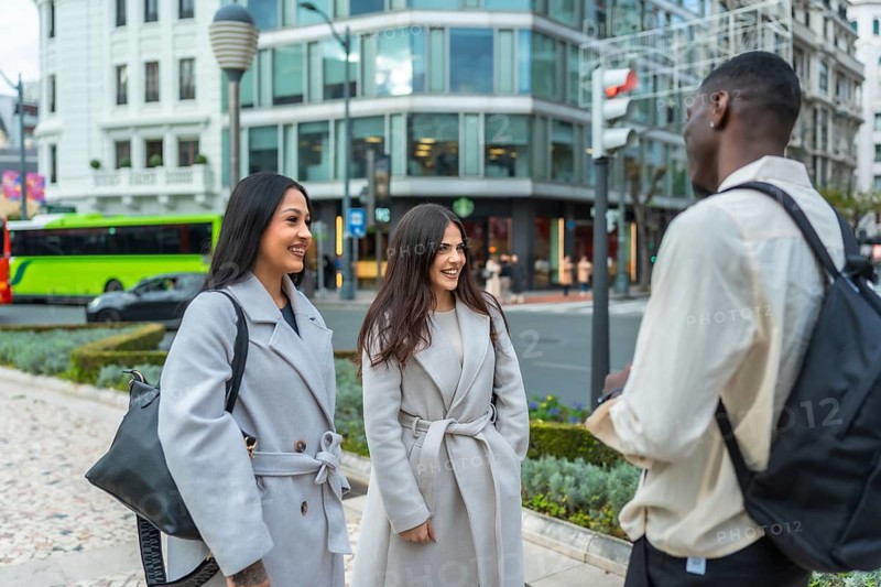 Young multiracial friends meeting on an urban street, engaging in a pleasant conversation, embodying concepts of connection, community, and social interaction in a modern city environment