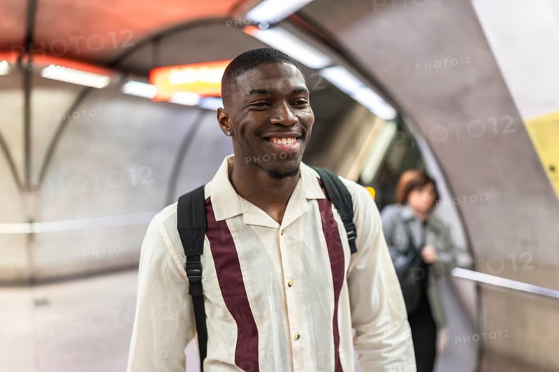 Smiling young african american man with a backpack walking through a modern underground subway station, enjoying his daily commute with a happy and positive expression