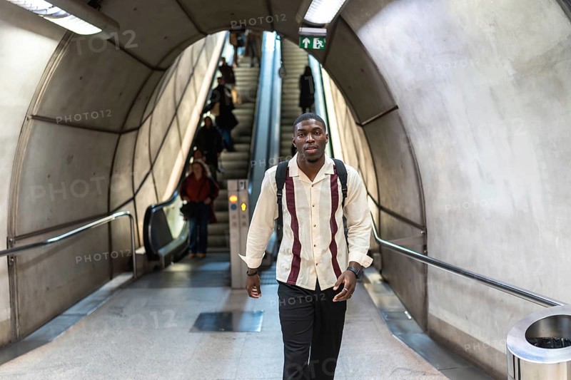 Young man with backpack walking confidently through a modern subway tunnel past escalators and commuters, capturing daily urban commute, public transit and purposeful movement