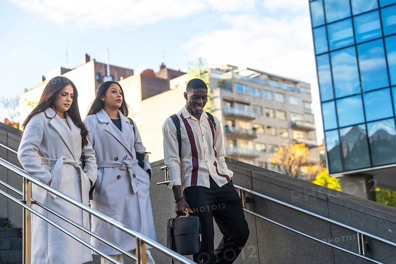 Three diverse business colleagues descending outdoor stairs, walking together after work or during a break, depicting office life, teamwork, and urban professionals