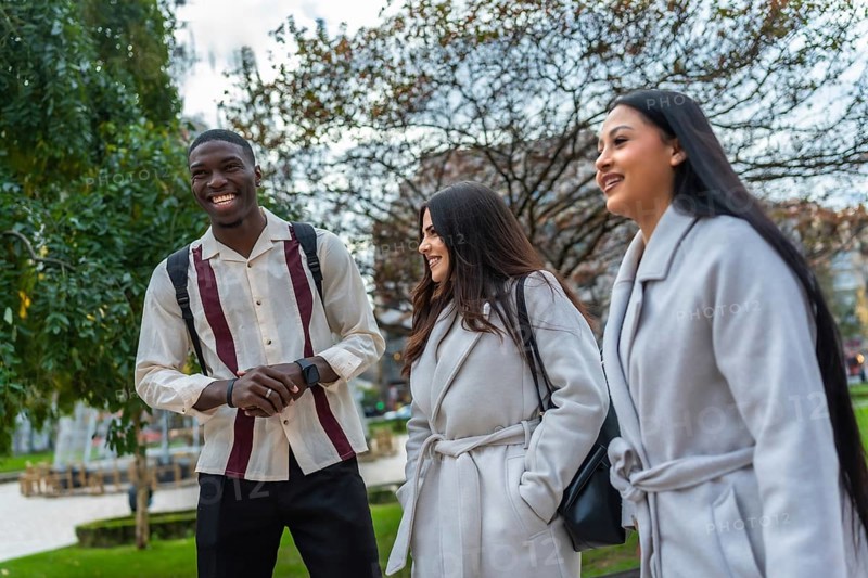 Multiracial young adults walking together in an urban park, smiling and happily conversing, showing friendship and a strong sense of community while connecting outdoors