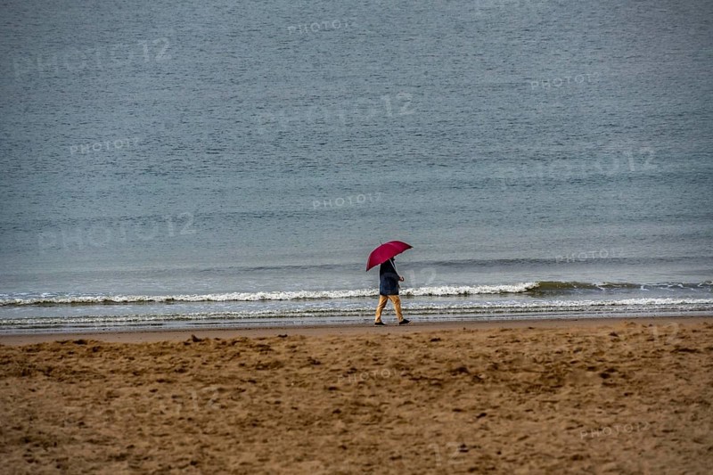 Person with red umbrella walking along the beach, calm sea in the background, winter break, on Zeedijk-Knokke, beach promenade in Knokke-Heist, beach walkers with umbrella when it rains, dreary winter day, Belgium