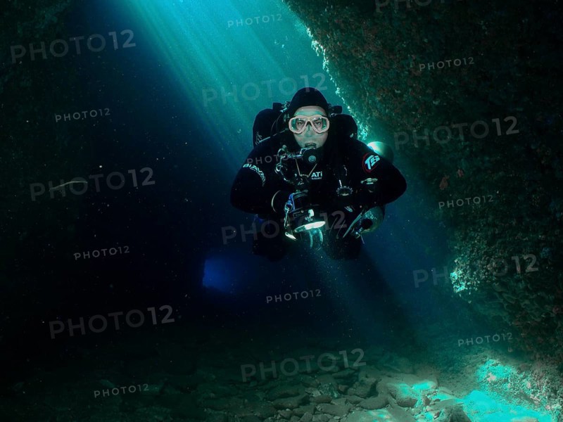 A diver with equipment floats through the interior of a blue-lit cave. Fraskeric dive site, Stoja, Pula, Croatia, Mediterranean