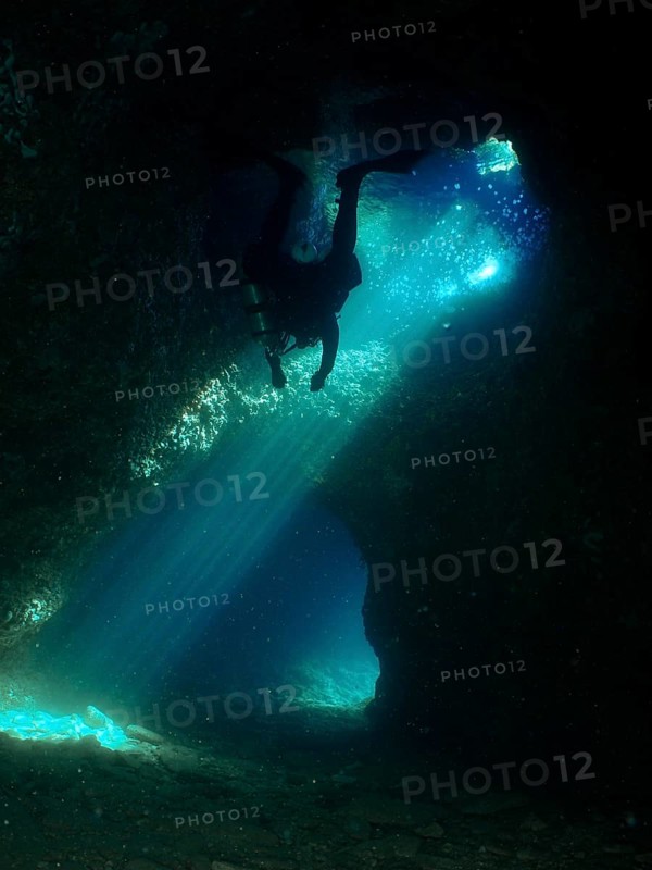 A dark cave is explored by a diver who is surrounded by dramatic rays of light. Fraskeric dive site, Stoja, Pula, Croatia, Mediterranean