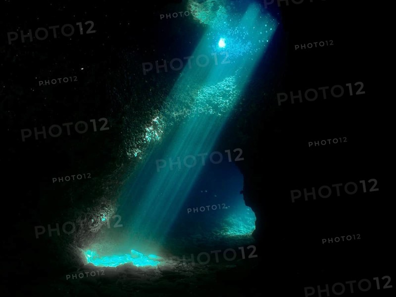 Sun rays illuminate the interior of a dark underwater cave with blue light reflections. Fraskeric dive site, Stoja, Pula, Croatia, Mediterranean Sea