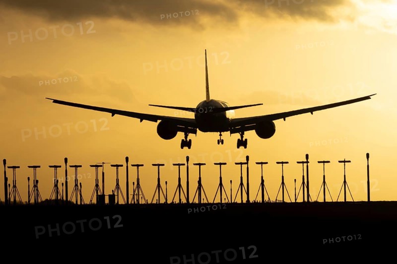 Boeing 777 commercial passenger jet aircraft in flight on approach to land over runway lights silhouette at sunset at London Stansted airport, Essex, England, United Kingdom