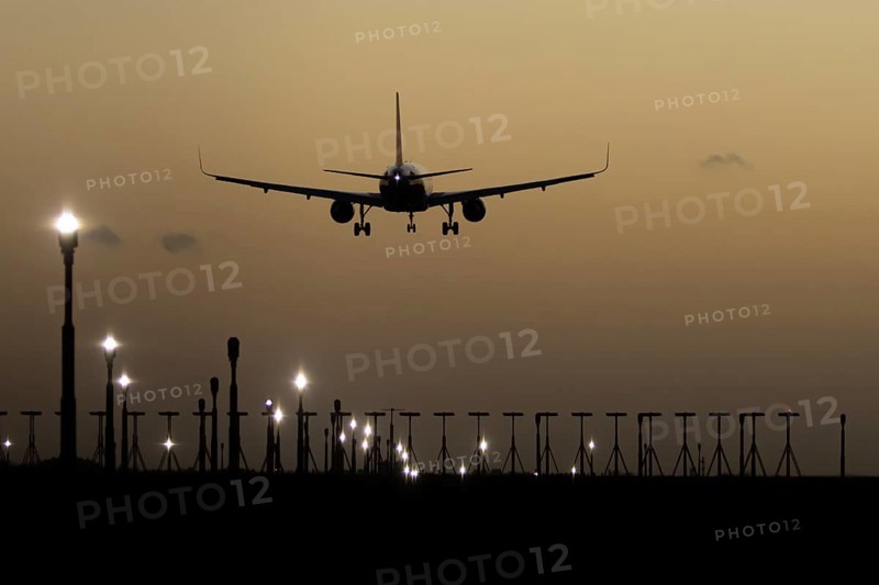 Airbus 320 commercial passenger airliner jet aircraft in flight on approach to land over runway lights at sunset at London Stansted airport, Essex, England, United Kingdom