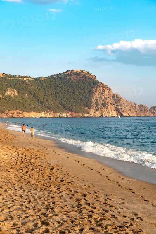 A couple walk along an empty Cleopatra Beach at sunset in the Turkish holiday resort town of Alanya on the Mediterranean coast of Turkey, the Turkish Riviera