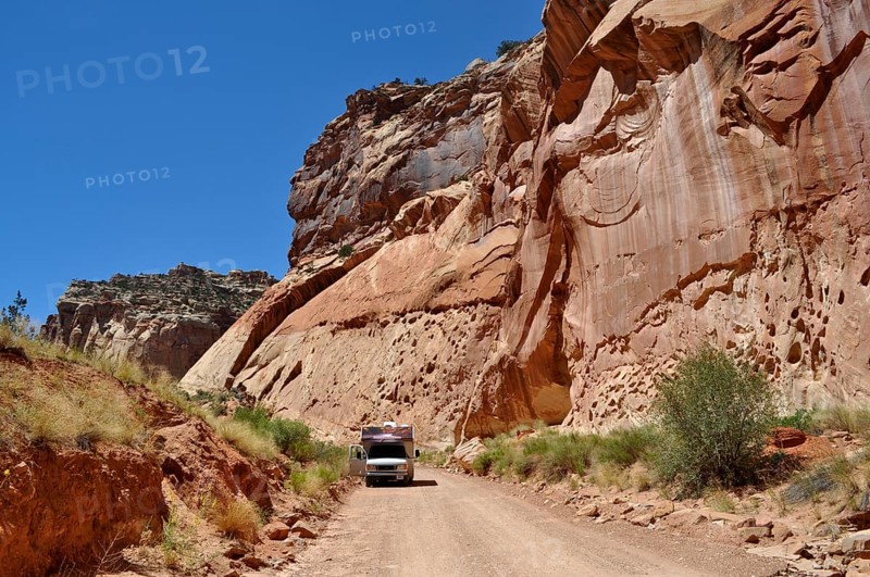A camper drives along a dirt road in a canyon with red rock walls, Capitol Reef National Park, Utha, USA