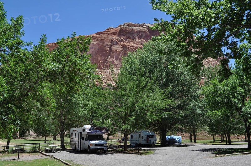 Motorhomes under trees at a campground in front of imposing red rocks, Fruita, Capitol Reef National Park, Utha, USA