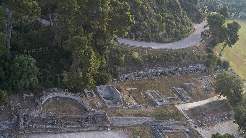 Old theatre and ruins next to a road surrounded by dense nature, drone shot, archaeological site, Ancient Olympia, Olympia, Peloponnese, Greece