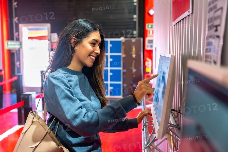 Young woman smiling while interacting with a touchscreen display, checking in for a karting session, representing leisure, entertainment, and modern technology