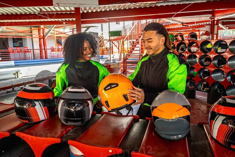 Diverse couple wearing racing suits and choosing helmets, standing on a go kart track, anticipating a fun and thrilling motorsport experience together