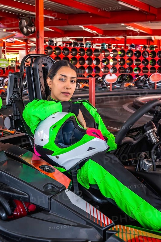 Young woman in a bright green racing suit holding a helmet and sitting in a go kart, ready for a race or practicing on the track, showcasing passion for motorsport